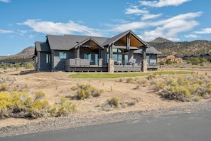 A modern two-story house with a large porch, a stone foundation, and a view of a hilly landscape.