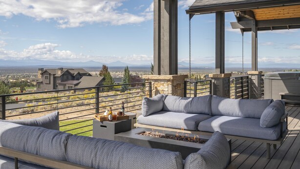 Een balkon met een bank en een vuurkorf, met uitzicht op een schilderachtig landschap met bergen en huizen.