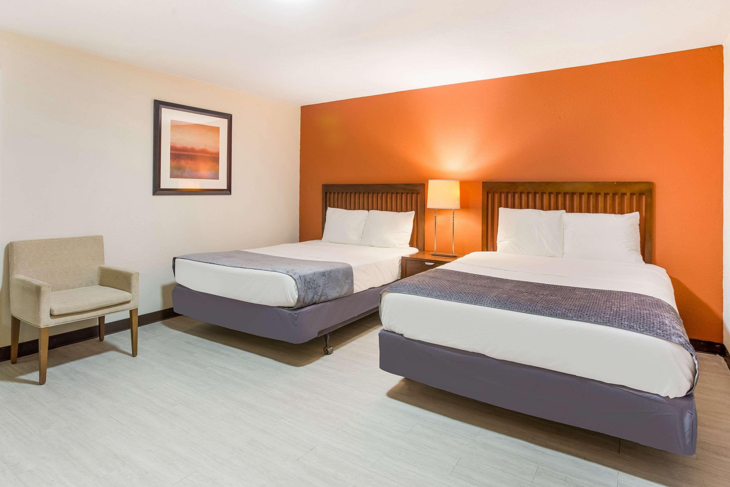 A hotel room with two beds, a chair, and a framed picture on the wall.