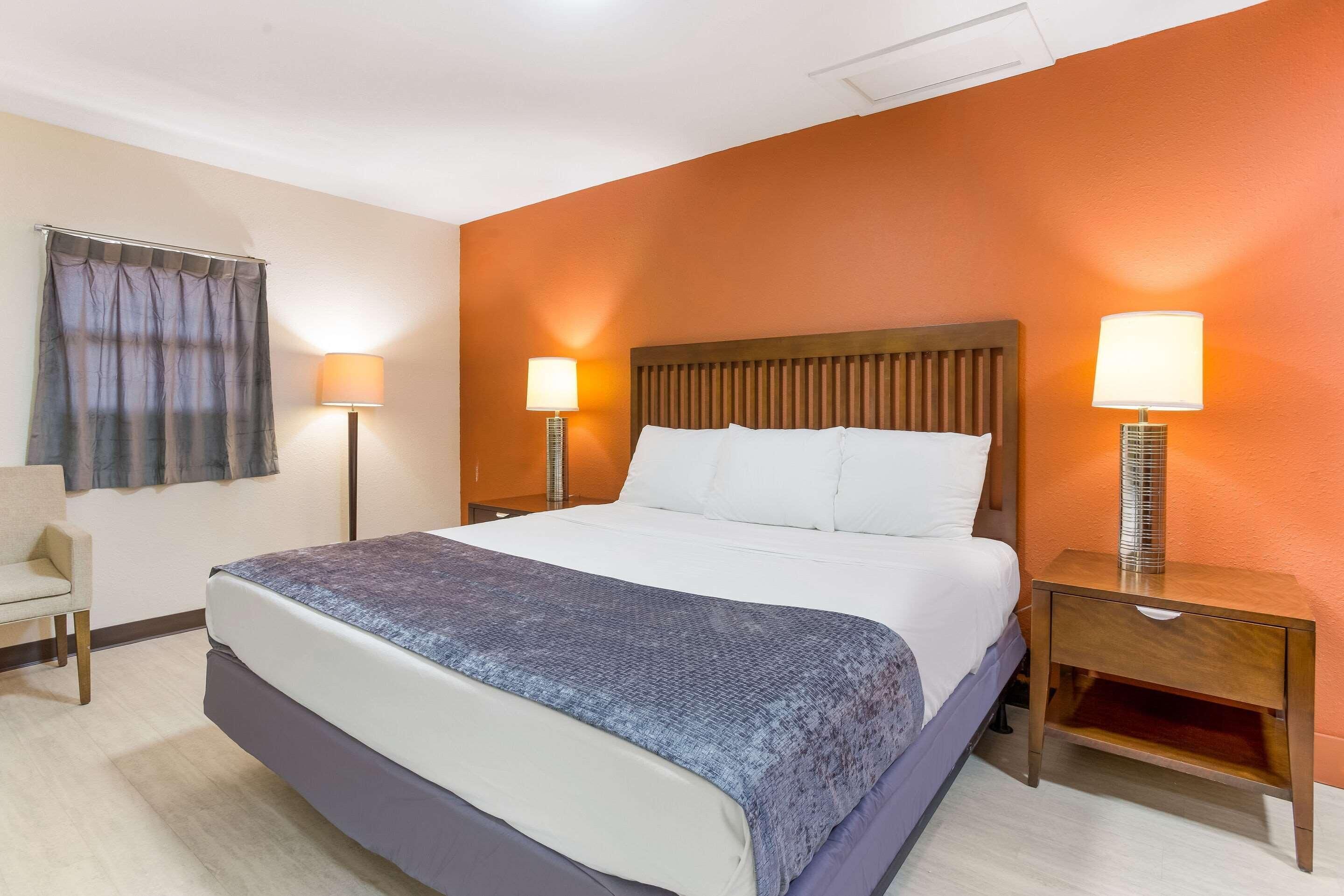 A hotel room with a bed, two bedside lamps, a chair, and a curtain.