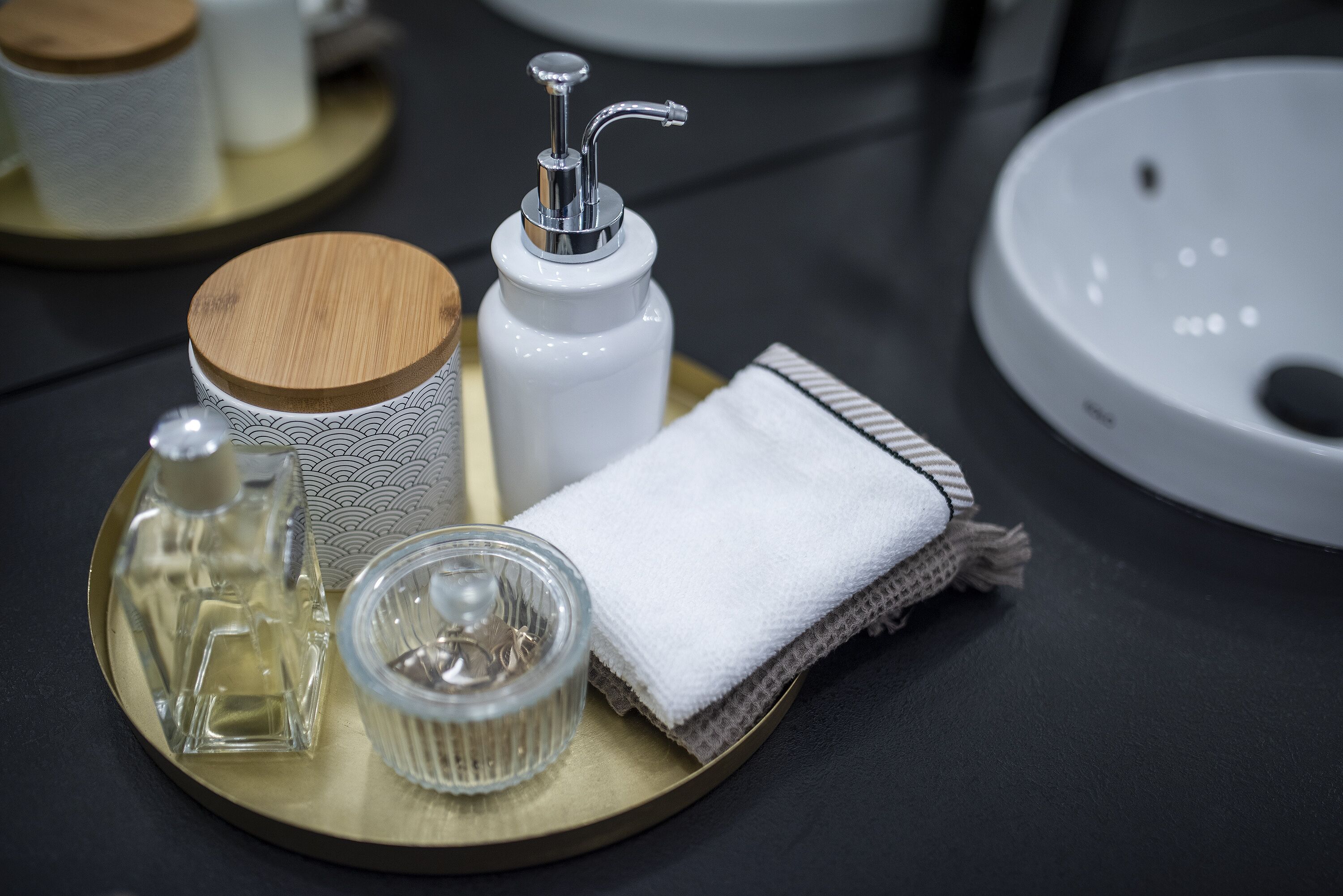 A tray with a soap dispenser, a bottle, a glass container, and a folded towel on a table.