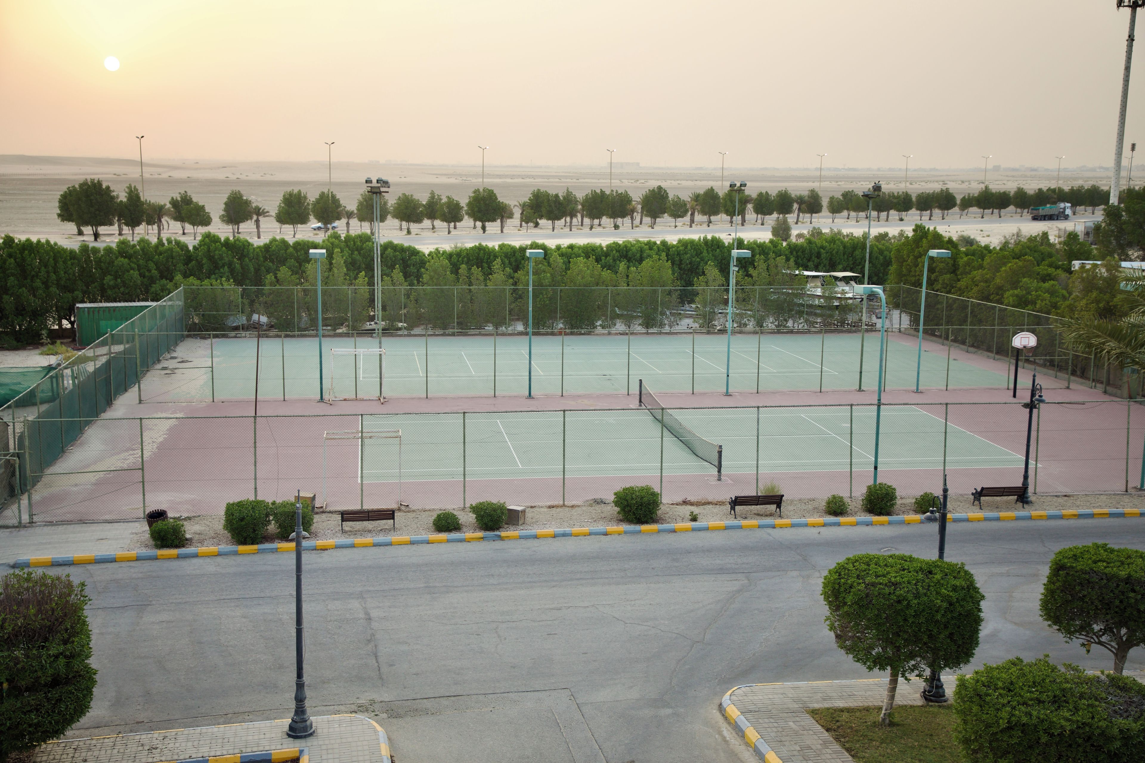 Un court de tennis en plein air, doté d’un filet, entouré d’arbres et de bancs.
