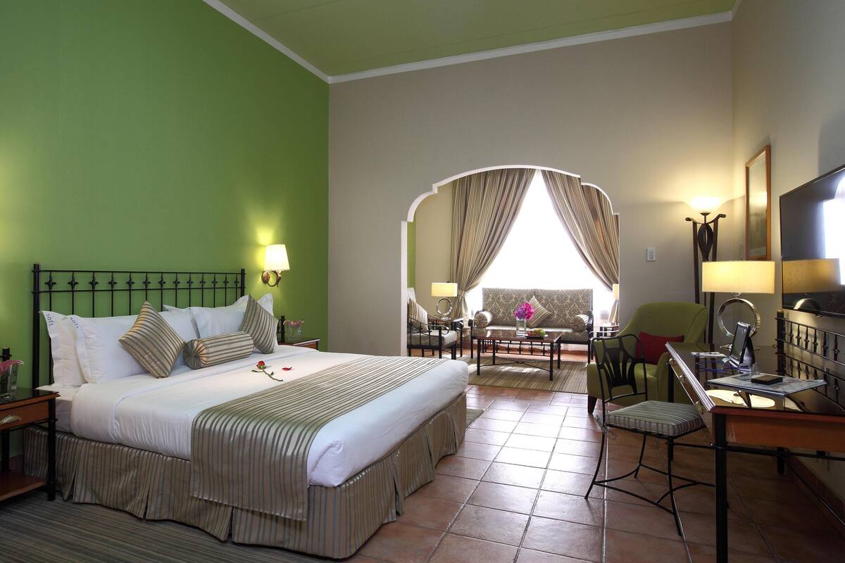 Une chambre d’hôtel avec un grand lit, un bureau avec une chaise, une télévision et une vue sur un balcon, accessible par une arche.