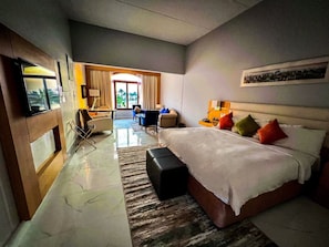 Ett hotellrum med en säng, ett skrivbord, en stol, en TV och utsikt över omgivningarna.