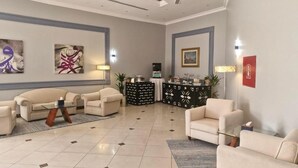 A hotel lobby with a reception desk, seating area with sofas and armchairs, artwork on the walls, and a tiled floor. - Mena Holiday Beach Resort Half Moon Bay (Dammam)