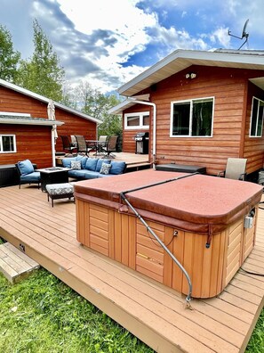 Une terrasse en bois avec un jacuzzi, du mobilier d’extérieur et un espace barbecue.