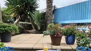 A patio with a table set for breakfast, surrounded by potted plants and a blue fence.