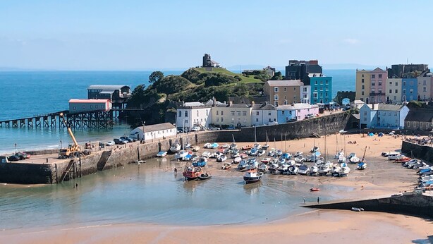 A coastal town with a sandy beach, a pier, and a variety of boats.