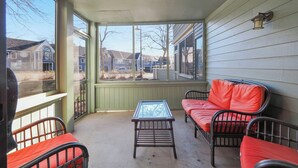 A covered porch with a glass-top table, two wicker chairs with red cushions, and a view of neighboring houses. - 103 Pointes North Inn | Downtown Charlevoix | Indoor/Outdoor Pool (Charlevoix)