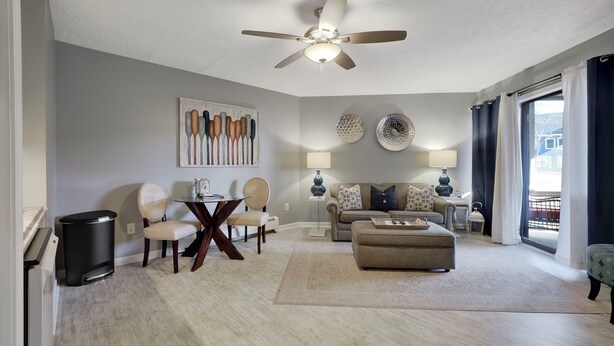A spacious living room with a ceiling fan, a dining area with a table and chairs, a sofa set, and a large window with curtains. - 103 Pointes North Inn | Downtown Charlevoix | Indoor/Outdoor Pool (Charlevoix)