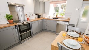 Una cocina moderna con armarios grises, horno empotrado, lavavajillas y un comedor con una mesa dispuesta para dos personas.