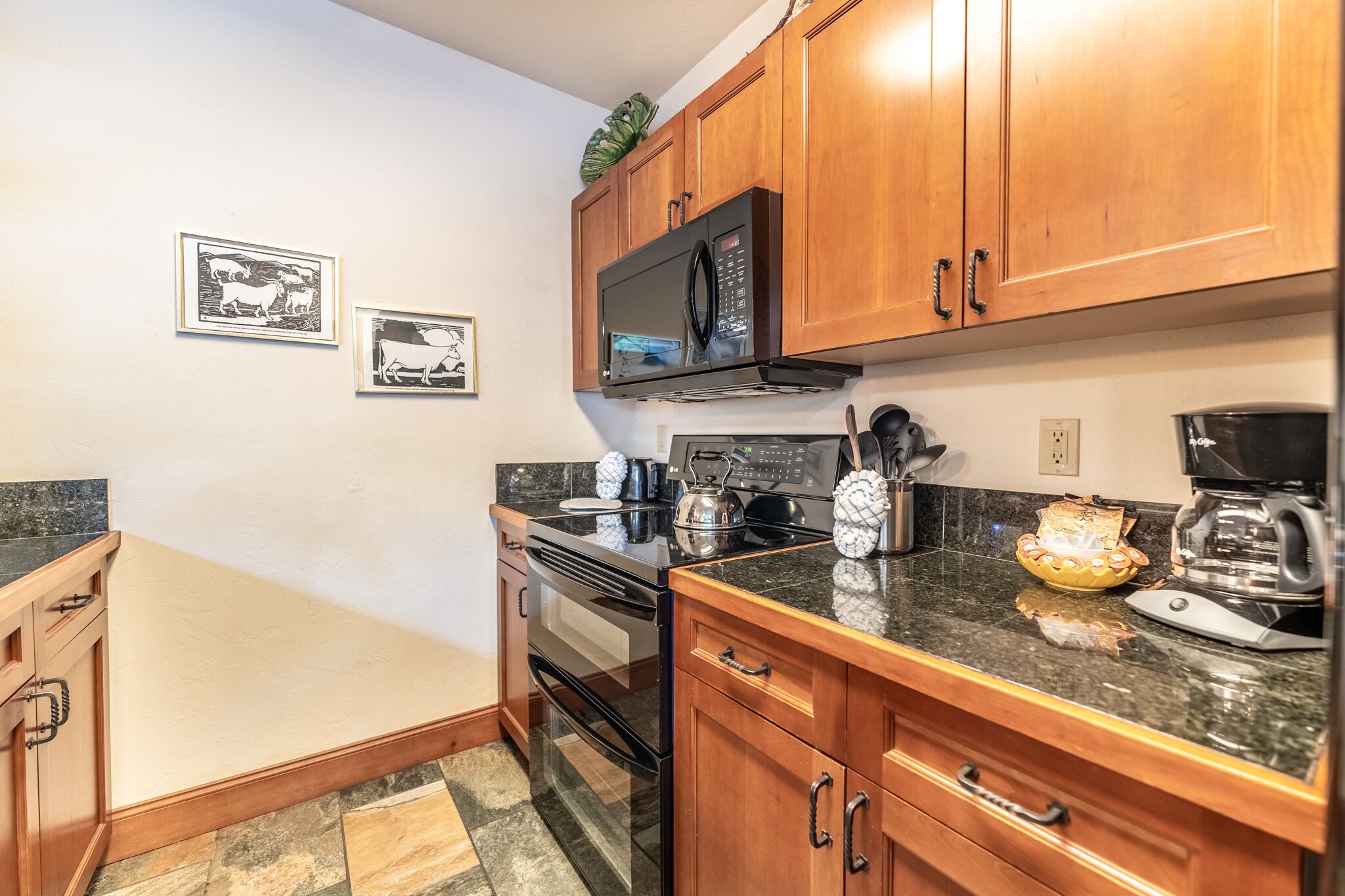 A kitchen with wooden cabinets, a microwave, an oven, and a coffee maker. There are framed pictures on the wall.