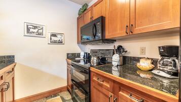 A kitchen with wooden cabinets, a microwave, an oven, and a coffee maker. There are framed pictures on the wall.