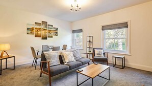 A living room with a sofa, coffee table, and chairs, a dining area with a table and chairs, and a large window with a view. - Host & Stay | The Captain's Loft (Whitby)