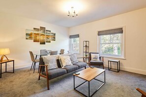 A living room with a sofa, coffee table, and chairs, a dining area with a table and chairs, and a large window with a view.