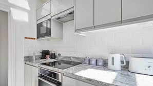 A modern kitchen with white cabinetry, a granite countertop, a built-in oven, a microwave, a coffee maker, and a toaster. - Host & Stay | The Captain's Loft (Whitby)