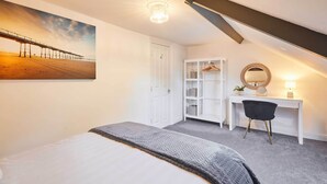 A bedroom with a bed, a desk with a chair, a wardrobe, a mirror, and a painting of a pier. - Host & Stay | The Captain's Loft (Whitby)
