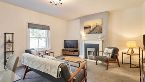 A living room with a sofa, a coffee table, a TV, a fireplace, and a bookshelf. - Host & Stay | The Captain's Loft (Whitby)