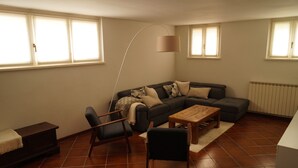 Ein Wohnzimmer mit Ecksofa, Couchtisch aus Holz, Stehlampe und Heizkörper.