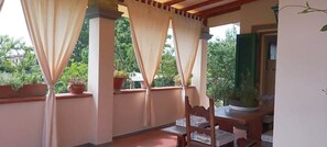 A balcony with a wooden chair, potted plants, and a view of greenery. - Villa El Rosal (Pietrasanta)