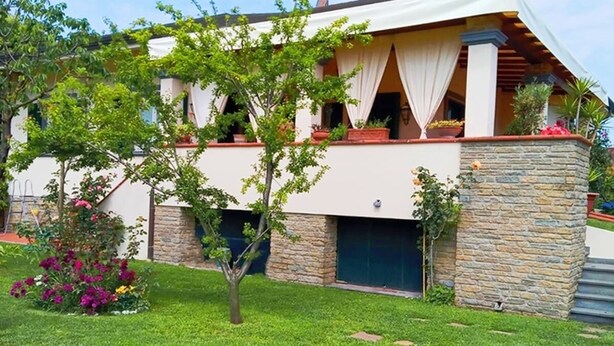 Ein modernes, zweistöckiges Haus mit Naturstein-Fassade, einem gepflegten Rasen und einem gepflasterten Weg zum Eingang.