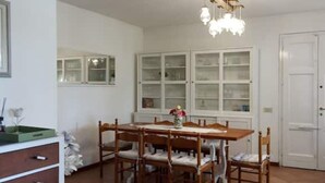 Ein Essbereich mit einem Holztisch, Stühlen, einer Chandelüster und einem weißen Schrank mit Glastüren.