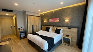 Una habitación de hotel moderna con una cama grande, mesitas de noche, un armario y una pequeña zona de estar.