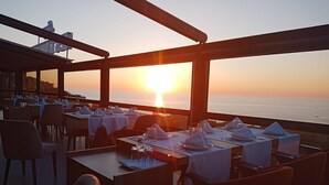 Un restaurante con mesas dispuestas para comer, con vistas a un atardecer sobre el mar.