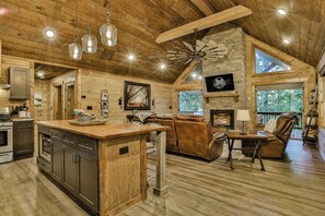 A rustic cabin interior with a kitchen, dining area, and living space. - Luxury Creekside~ Hot Tub | Game Room | Fire Pit | Sleeps 8 (Ellijay)
