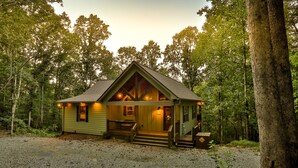 Eine kleine, eingeschossige Holzhütte mit Veranda und Essbereich, umgeben von Bäumen.