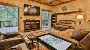 Ein gemütliches Blockhausschlafzimmer mit Holzvertäfelung, einem großen an der Wand montierten Fernseher, Ledersofas und einem Tablet, das ein Spiel zeigt.