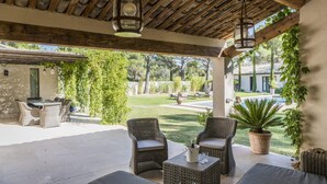 An outdoor patio area with wicker furniture, a table with a bottle and glasses, and a view of a pool and garden. - Vacation rental house with pool LOURMARIN LS2-385 (Lourmarin)
