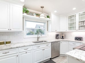 A modern kitchen with white cabinetry, a stainless steel dishwasher, and a window providing natural light. - A Salty Senorita | Luxurious + Beachfront Sunsets + Game Room! (Tybee Island)