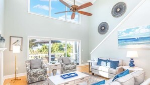 Amplia sala de estar con ventilador de techo, dos sofás, una mesa de centro y un gran ventanal con vistas a un balcón.