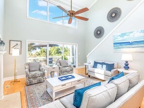 A spacious living room with a ceiling fan, two sofas, a coffee table, and a large window overlooking a balcony. - A Salty Senorita | Luxurious + Beachfront Sunsets + Game Room! (Tybee Island)