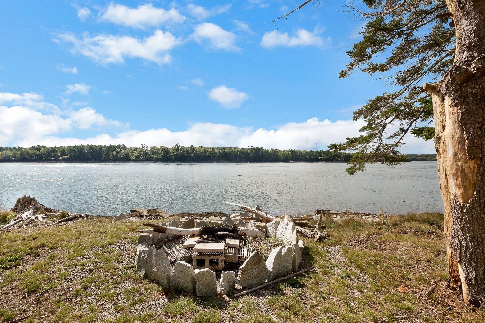 A lakeside campsite with a fire pit, surrounded by rocks and trees.