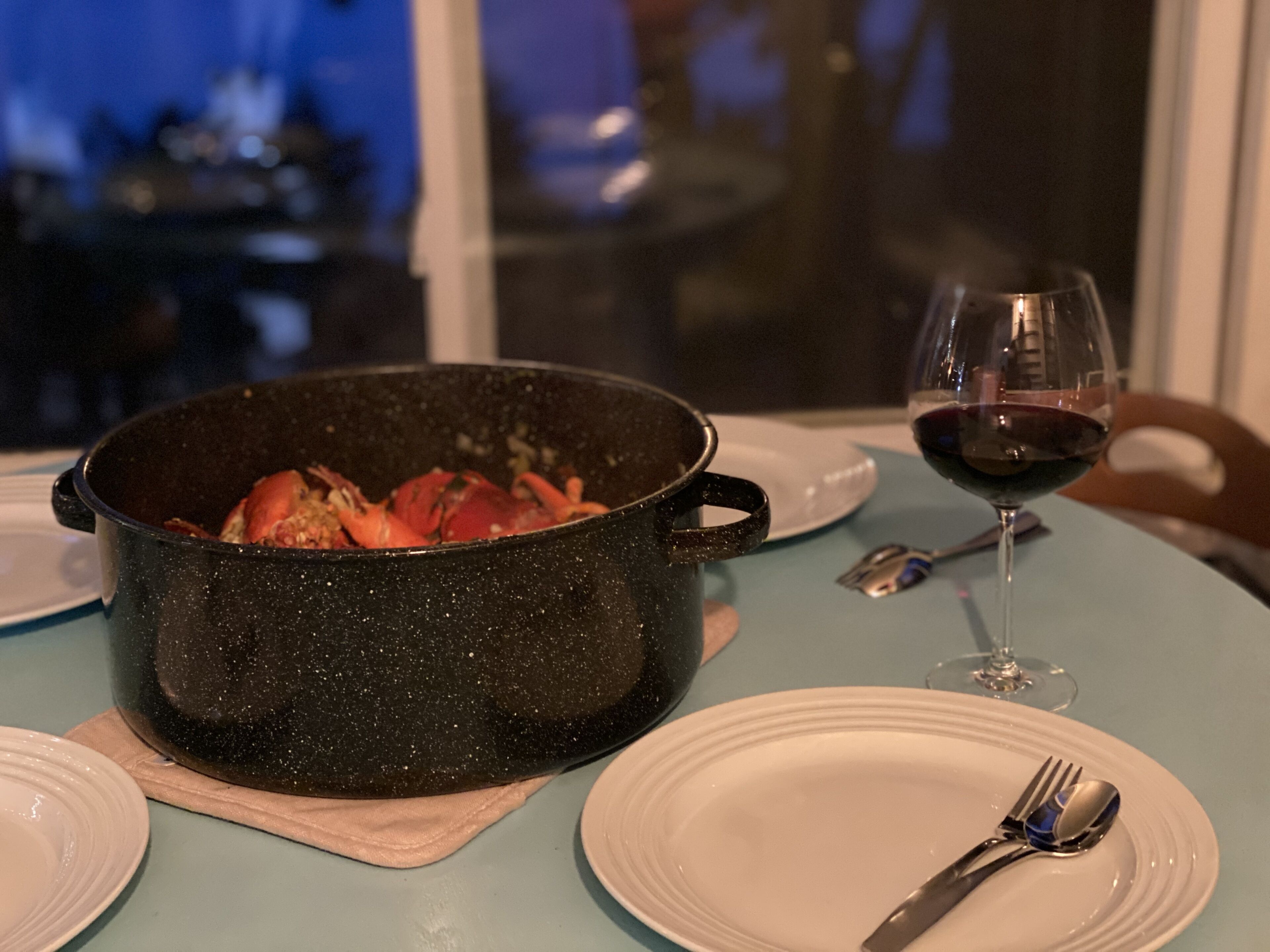 A dining table with a black pot containing food, a wine glass with red wine, and dining utensils.