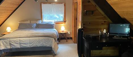 A cozy attic bedroom with a bed, desk, and computer.