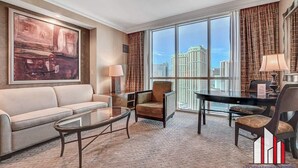 A hotel room with a large window, a sofa, a coffee table, and a dining table with chairs.