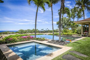 A pool area with clear blue water, surrounded by tropical vegetation and palm trees, with a view of the ocean. - Exquisite 4BR Hainoa Estate 122 at Hualalai – Ocean Views & Infinity-Edge Pool (Kailua Kona)