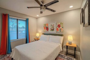 A bedroom with a bed, two bedside lamps, a ceiling fan, and a window with blinds.
