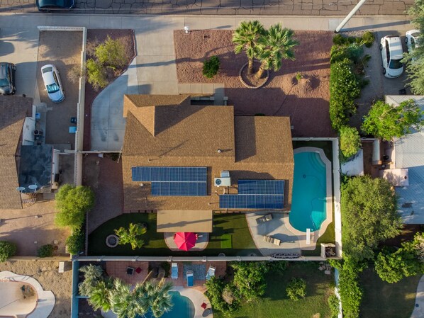 An aerial view of a residential property with a swimming pool, solar panels, and a driveway with parked cars. - Modern 3BR Resort w/ Private Pool & Putting Green (Scottsdale)