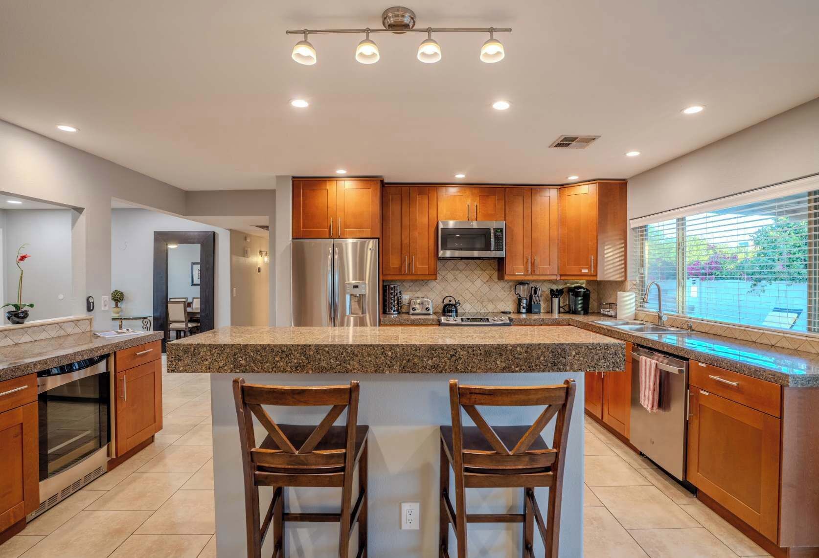 A modern kitchen with granite countertops, stainless steel appliances, wooden cabinets, and a large island with bar stools.
