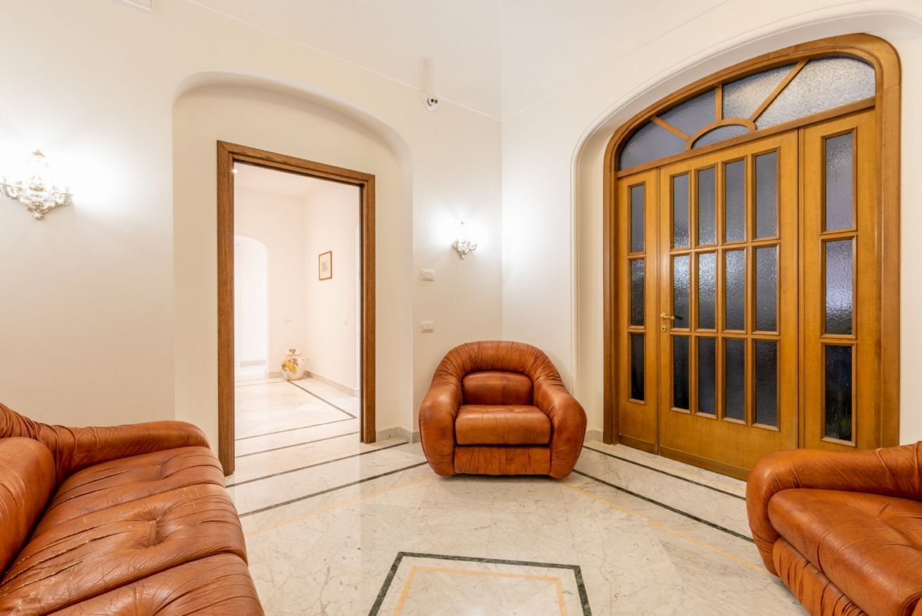 A spacious lobby with a leather armchair, a wooden door with glass panels, and a marble floor.