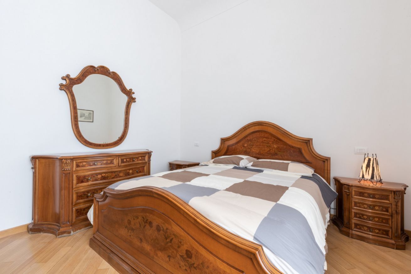 A bedroom with a wooden bed, a dresser, a nightstand, and a mirror.