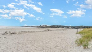 A sandy beach with a clear sky and distant buildings.