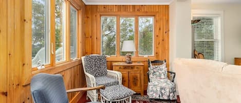 Una habitación acogedora con paredes de madera, un tapete rojo estampado, un sofá y dos sillones con tapicería floral.
