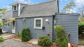 A two-story house with a gray exterior, a front door, a small window, and a chimney.