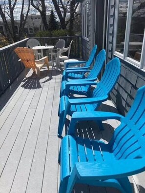 A deck with blue Adirondack chairs and a small table with chairs.
