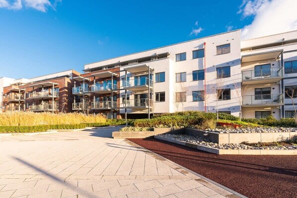 A modern apartment building with multiple balconies, a landscaped courtyard, and a clear sky.